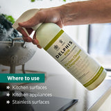 Bottle of Delphis Eco kitchen cleaner being held over a kitchen surface with text indicating where to use it.