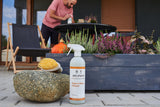 Delphis patio and stone cleaner bottle on a patio with plants and a person in the background